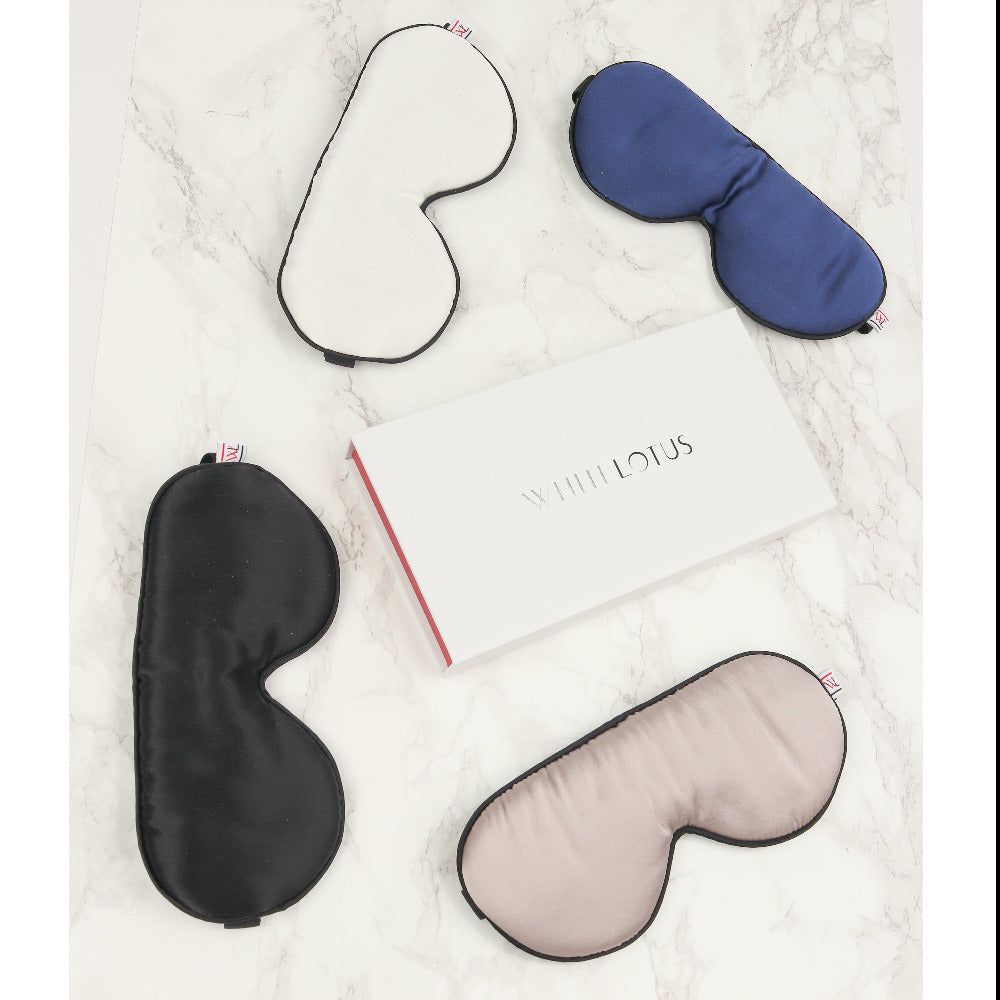 A photo of a navy, black, white and pearl grey eye mask on a marble background with a white lotus box